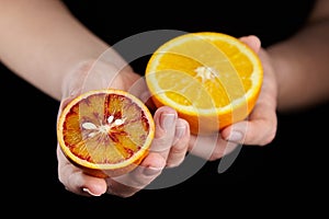 Orange and blood or red orange fruit halves in hands on black background