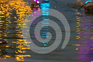 Orange, blue, purple reflections on the water surface with waves from a shouldering fountain. A walk in the evening