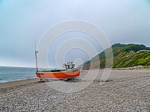 Orange boat on british shingle beach with mountain background