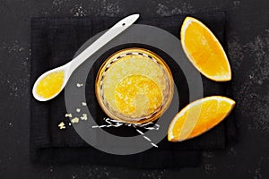 Orange body scrub with sugar and coconut oil in glass jar on black table from above. Homemade cosmetic for peeling and spa care