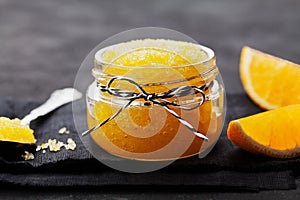 Orange body scrub with sugar and coconut oil in glass jar on black table. Homemade cosmetic for peeling and spa care