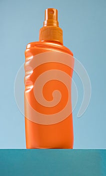Orange bottle of sunscreen on the podium on a blue background. Summer time on the beach with sun cream.