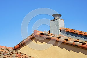 Orange building exterior with adobe red roof tiles and white stone chimney with metal vent and clear blue sky background