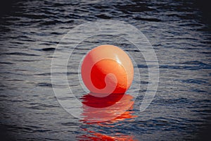 Orange buoy floating on dark dramatic sea water