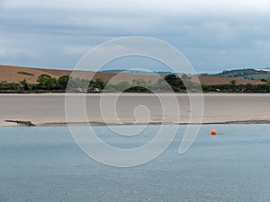 A orange buoy on a water surface. The sandy shore of the sea bay. The coastline on a cloudy day. Seaside landscape