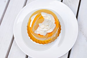 Orange cake on white plate and wooden table with cream and a pie