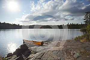 Orange canoe on rocky shore of Boundary Waters lake near sundown