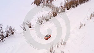 Orange car is driving along a winter snowy country road. Aerial view from the drone.