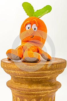 Orange carrot plush toy sitting on a pillar against white studio background