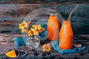 Orange and carrot smoothie in glass bottles with stainless straw and crystal small vases with Chernobrivtsi flowers and