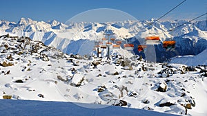 Orange chairlift with unrecognizable skiers in Samnaun - Ischgl - Paznaun ski resort, located in Austria and Switzerland