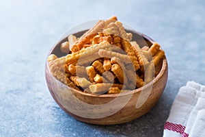 Orange Cheese Flavored Corn Snacks in Stick Shape / Roasted Chips or Salty Crackers in Wooden Bowl.