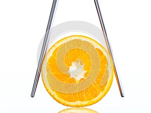 Orange in chopsticks on white background.