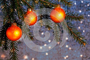 Orange Christmas ornaments on spruce branches on a shiny blue-silver background. New Year`s or Christmas background