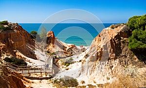 Orange cliffs, blue sea, footbridge, beach  in `Falesia` in Algarve, Portugal