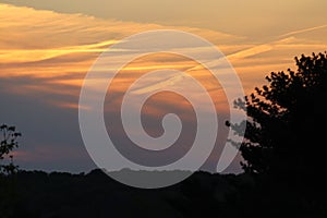 beautiful orange sunset over trees streaking clouds