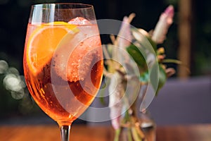 Orange cocktail with orange garnish in wine glass, aperol spritz in sunny setting
