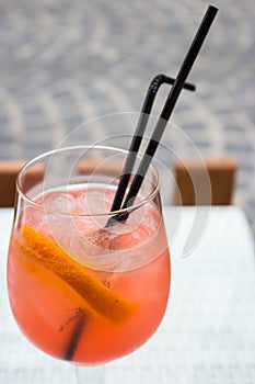 Orange cocktail with ice and two straws. Aperol spritz cocktail on table. Drinks in outdoor bar. Summer party background.