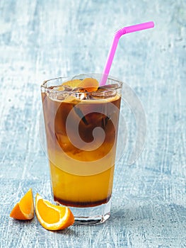 Orange cold coffee with ice cubes on blue stone background