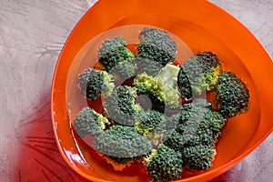 An orange color bowl with broccoli florets immersed in water