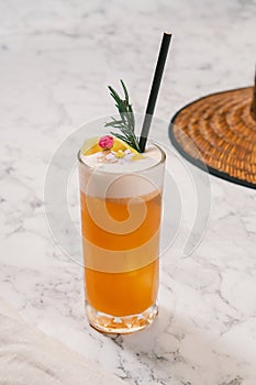 An orange color cocktail in a highball glass decorated with orange peel.