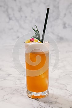 An orange color cocktail in a highball glass decorated with orange peel.