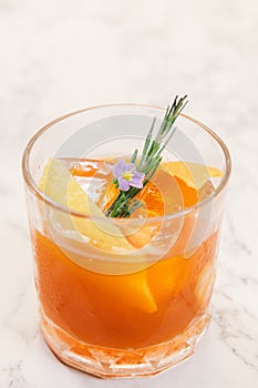 An orange color cocktail in a rocks glass decorated with orange peel, rosemary.