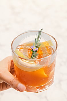 An orange color cocktail in a rocks glass decorated with orange peel, rosemary.