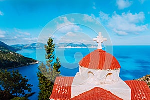 Orange colored Hellenic shrine Proskinitari on the cliff edge with defocused sea and cloudscape view in the background