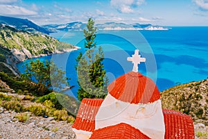 Orange colored Hellenic shrine Proskinitari on the cliff edge with defocused sea and cloudscape view in the background