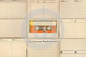 Orange compact cassette in front of tape boxes with empty labels