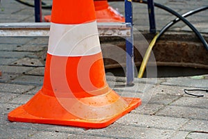 Orange cones installed around the dangerous area on the sidewalk. An open travel hatch. Laying of a new fiber-optic cable in the