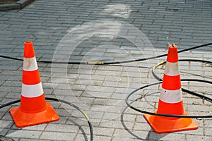 Orange cones installed around the dangerous area on the sidewalk. An open travel hatch. Laying of a new fiber-optic cable in the