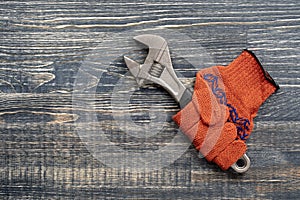 Orange construction gloves in which the monkey wrench is clamped. Tool kit, monkey wrench and work gloves on wooden background,