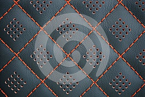 Orange contrast thread on perforated natural black leather car seat close-up