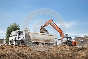 Orange crawler excavator and gray dump truck during excavation phase at construction site. Bottom view