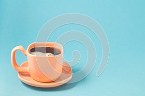 orange cup with black coffee on a blue background/ orange cup of espresso with a skin on a blue background with copy space