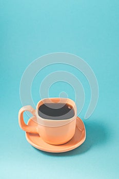 orange cup coffee on a blue background/orange cup with a saucer full of black coffee on a blue background with copyspace