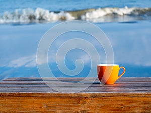 Orange cup of coffee on brown wooden table on beach