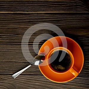 Orange cup of coffee on dark wooden background.