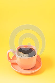 Orange cup with a saucer full of black coffee on a yellow background/orange cup of espresso with a skin on a yellow background