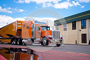Orange custom semi truck big rig trailer drive on truck stop