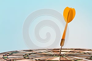 Orange dart arrow hitting bulls-eye in center of dartboard on blue sky background
