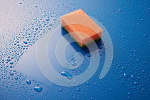 Orange double sided cleaning sponge paled on blue background covered with drops with copyspace