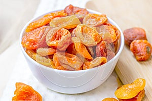 Orange dried apricots in white bowl on light background.