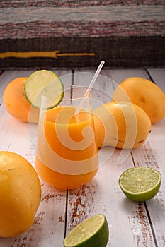 Orange drink closeup with lime slice on white vintage wooden desktop with mangos