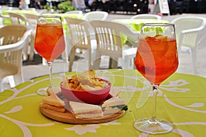 orange drink glasses, drink appetizers,triangular sandwiches and chips, drink snack, classic Italian alcoholic drink, outdoor