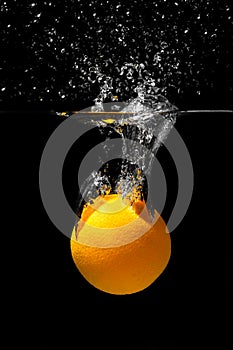 Orange drowns in water on a black background. Citrus with water splashes