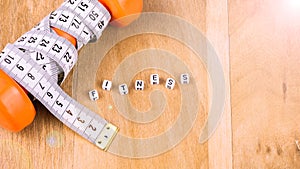 Orange dumbbell with centimetric tape and fitness cube letters on wooden background