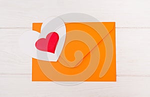 Orange envelope and two hearts on a white wooden background